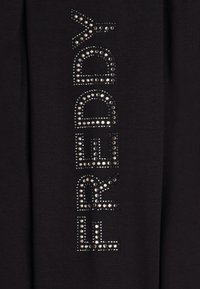Tessuto nero con grande scritta "FREDDY" in borchie argentate. Le lettere presentano un design arrotondato, creando un contrasto visivo testurizzato.