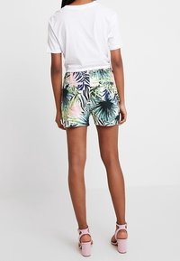 Blommönstrade shorts i gröna, rosa och blå nyanser, gjorda av lättviktsmaterial. Kombineras med en vit t-shirt och rosa klacksandaler.