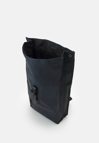 Tmavomodrý batoh vyrobený z vodotesného materiálu, s horným otvorom, vonkajším zip vreckom a nastaviteľným popruhom vpredu.