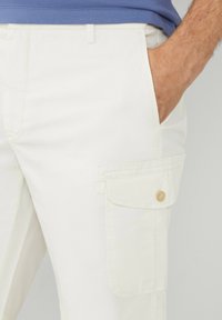 Pantaloni cargo bianchi con tasca laterale, dotati di chiusura a bottone. Realizzati in tessuto leggero con una superficie liscia.