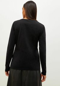 Svart långärmad tröja med rundad halsringning, slät textur, figurnära design och platta sömmar, i kombination med en svart läderskjol.
