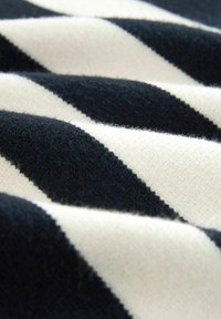 Tissu présentant de larges rayures diagonales noires et crème ; surface douce et texturée avec des fibres visibles et une apparence chaleureuse.