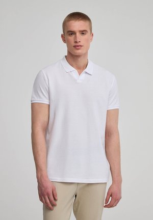 Polo bianco a maniche corte, con un piccolo colletto, texture a coste e orlo dritto. Indossato con pantaloni khaki.