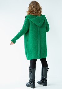 Zielona dzianinowa, oversize'owa bluza z kapturem, z prążkowanymi mankietami i dołem. Noszona z czarnymi legginsami i czarnymi kozakami za kolano z klamrami.