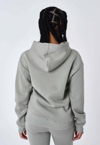 Lichtgrijze oversized hoodie met een trekkoordcapuchon, ribgebreide manchetten en zoom. De stof lijkt zacht met een gladde textuur.