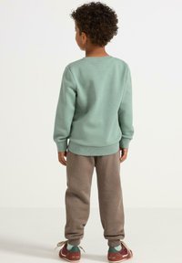 Mintgrüner Pullover mit gerippten Bündchen, kombiniert mit hellbraunen Jogginghosen. Das Outfit wird durch burgunderrote Sneakers mit Schnürsenkeln ergänzt.