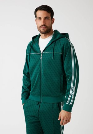 Sudadera verde con cremallera y un patrón texturizado, líneas blancas en los hombros y marca en el brazo izquierdo. Cuenta con cordones ajustables.