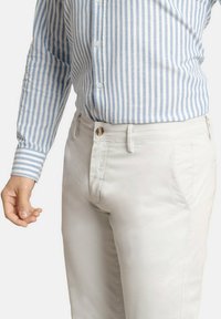 Camisa de botones a rayas azul claro y blanca combinada con chinos color crema, de corte clásico y textura sutil.
