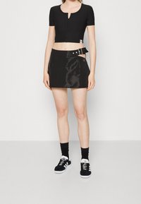 Crop top noir avec un col en trou de serrure, associé à une mini-jupe noire brillante avec une boucle sur le côté. Baskets noires avec des accents blancs.