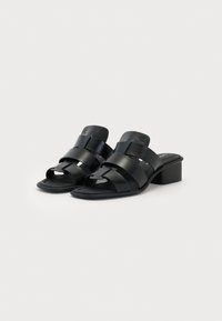 Sandales noires avec un talon bloc et plusieurs larges sangles. Le matériau semble lisse et légèrement brillant, avec un design à bout ouvert.