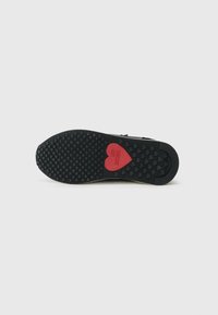 Semelle en caoutchouc noir présentant un motif de bande de roulement texturé et un accent en forme de cœur rouge avec "LOVE MOSCHINO" embossé à l'intérieur.