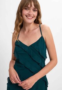 Türkises Kleid mit dünnen Trägern, das überlagerten Rüschen entlang des Oberteils und einem V-Ausschnitt verfügt, aus einem leichten, fließenden Stoff gefertigt.