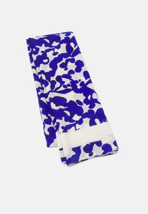 Tissu blanc plié avec un motif floral abstrait bleu sur un fond clair uni.