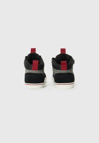 Black high-top sneakers with red pull tabs, grey accents, and white soles. Textured suede and fabric materials create contrast in design.