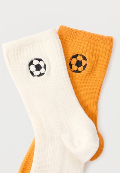 Λευκές και πορτοκαλί ριγωτές κάλτσες με κεντημένες ασπρόμαυρες ποδοσφαιρικές μπάλες κοντά στα πάνω μανσέτα.