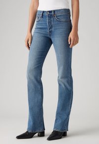 Bågade blå jeans i medelblå denim, med hög midja, klassisk femfickdesig och subtilt fransad fåll med mörka detaljer.