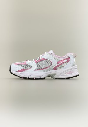 Baskets blanches et roses avec des panneaux en mesh, des lacets et une semelle épaisse, positionnées de profil sur un fond neutre.