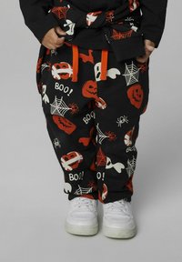 Zwarte katoenen broek met Halloween-thema prints: pompoenen, geesten, spinnenwebben en spinnen in rood en wit. Voorzien van oranje trekkoorden.