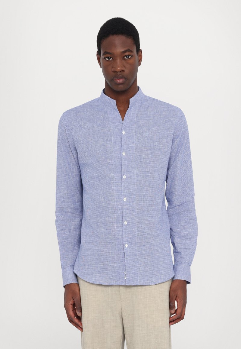 Camicia azzurra chiara a maniche lunghe con colletto a serafino, chiusura con bottoni e tessuto texturizzato. La camicia presenta un delicato motivo tessuto e una vestibilità aderente.