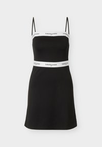 Μαύρο μίνι φόρεμα χωρίς μανίκια με λεπτές τιράντες, λευκές ταινίες στο στήθος και τη μέση με το λογότυπο "tommy jeans" σε μαύρο κείμενο.