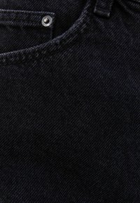 Tela de mezclilla negra con una textura suave, que presenta costuras visibles y un acento de botón metálico cerca de la parte superior.