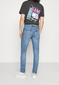 Blå denimjeans med slim fit, med en bakre läderpatch och subtila sömnadsdetaljer, kombinerat med en svart grafisk t-shirt.