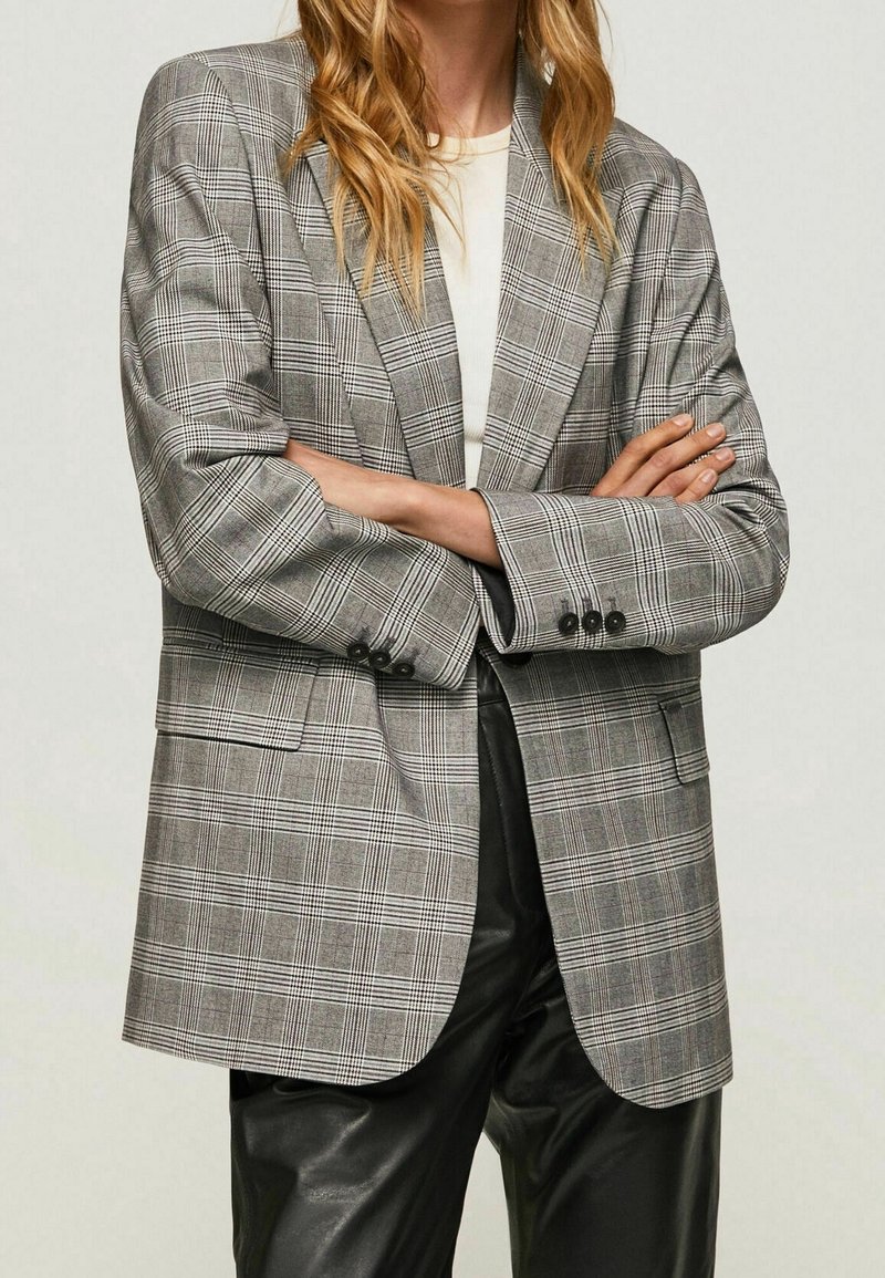 Blazer de cuadros gris con un diseño elegante, que presenta un cierre de un solo botón, solapas de muesca y puños abotonados, combinado con pantalones de piel sintética negros.