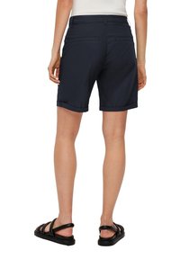 Shorts bleu marine en tissu léger, avec un ourlet replié, des poches arrière et une ceinture standard. Portés avec des sandales noires.