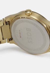 Reloj chapado en oro con caja redonda y pulsera de metal. La parte trasera grabada muestra "BOSS", resistente al agua hasta 5 bares y con detalles de acero inoxidable.
