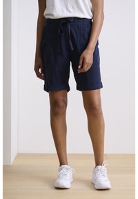 Pantaloni corto di cotone blu navy con risvolti, vita elasticizzata e tasche frontali, abbinati a scarpe da ginnastica bianche.