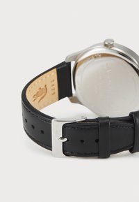 Svart läderarmband med silvermetallspänne, med en slät yta och perforeringar. Klockkapsel i rostfritt stål med en polerad yta.