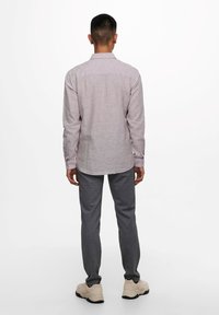 Camisa de manga larga gris claro con cuello abotonado, combinada con pantalones oscuros ajustados gris oscuro y zapatillas crema. Diseño sencillo, sin patrones.