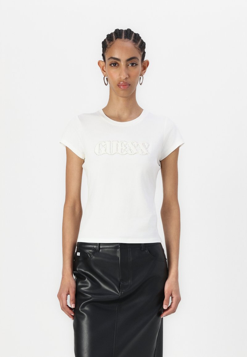 Hvit kortermet t-skjorte med "GUESS" logo i teksturert detaljering. Kombinert med et svart skinnskjørt. Glatt stoff, design med rund hals.