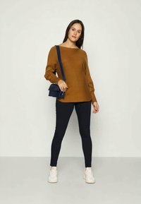 Brown textured sweater with a loose fit, worn with black skinny jeans and white sneakers. The model carries a small navy crossbody bag.