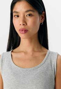 Grijze geribbelde tanktop met een wijde halslijn en een zachte textuur, voorzien van subtiele horizontale lijnen, gedragen door een model met lang zwart haar.