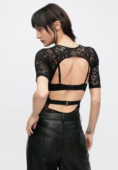 Fekete csipkés body rövid ujjakkal, nyitott háttal és elasztikus pántokkal. Fekete bőr nadrággal párosítva, melynek hátul zsebei vannak.