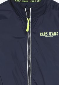 Námořnická větrovka s vysokým límcem, bílým zipem a žlutým táhnutím. Na prsou je logo "CARS JEANS" v limetkově zelené barvě.