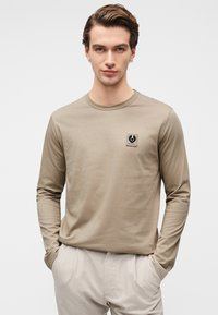 Μπεζ μακρυμάνικο t-shirt από βαμβάκι, με μικρό μαύρο λογότυπο στο αριστερό στήθος και σχέδιο με στρογγυλή λαιμόκοψη.