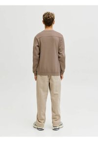Sudadera marrón con cuello redondo y mangas largas, combinada con jeans beige claros. El conjunto tiene un corte relajado y un diseño minimalista.