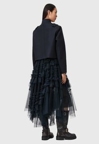 Giacca cropped blu navy con bottoni sulle spalle, gonna a strati in tulle nero con dettagli di rouches, abbinata a stivali neri fino al polpaccio.