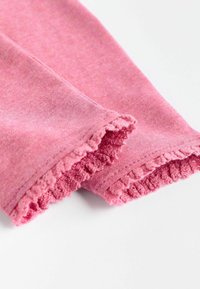 Roze leggings met een getextureerde, gerimpelde zoom. Zacht materiaal met een licht gemêleerd uiterlijk, met een close-up van het detail van de boord.