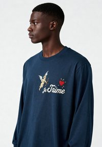 T-shirt à manches longues de couleur marine avec un motif brodé représentant Cupidon, un cœur, le soleil, et la phrase "Je t'aime" en écriture blanche sur la poitrine.