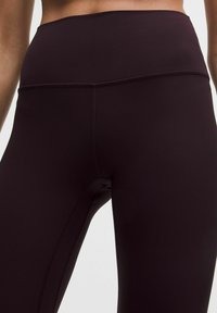 Visoko pas strani, elastične burgundske legice z gladko teksturo in flatlock šivi za udobje in vzdržljivost. Brez vidnih logotipov ali vzorcev.