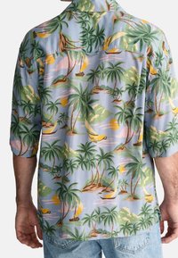 Modrá košile s krátkým rukávem na knoflíky, zdobená tropickým potiskem palem a pláže v zelené, žluté a růžové barvě. Měkká tkanina, volný střih.