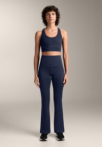 Granatowy stanik sportowy i pasujące legginsy z wysokim stanem i rozkloszowanym dołem, wykonane z elastycznego materiału, charakteryzujące się gładką teksturą i minimalną ilością szwów.