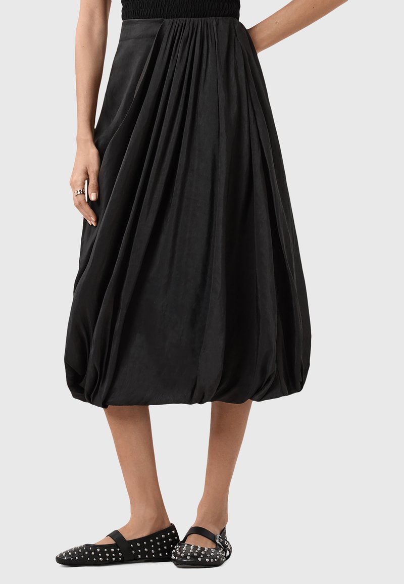 Gonna nera a palloncino con design plissettato; il tessuto leggero crea volume. Un paio di ballerine nere con borchie completa il look.