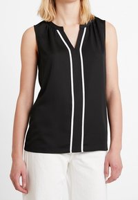 Blouse noire sans manches avec un col en V, présentant des rayures blanches verticales sur le devant et des détails plissés au niveau de l'encolure. Tissu lisse.
