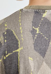 Graues, gemustertes T-Shirt aus Stoff mit abstrakten schwarzen und gelben Designs, geripptem Ausschnitt und weicher Textur. Ansicht von hinten.
