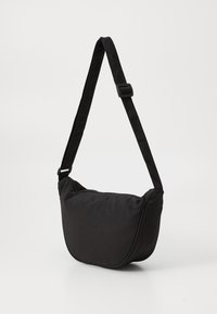 Saco de tecido preto com forma curva, alça ajustável e fecho de zipper. Apresenta uma textura suave e detalhes de costura nas bordas.