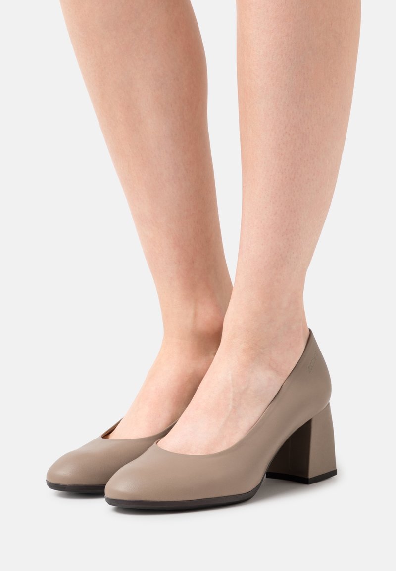 Chaussures à talons hauts en cuir beige avec un bout rond, un talon bloc de hauteur moyenne, une texture lisse, et un marquage subtil à l'arrière.